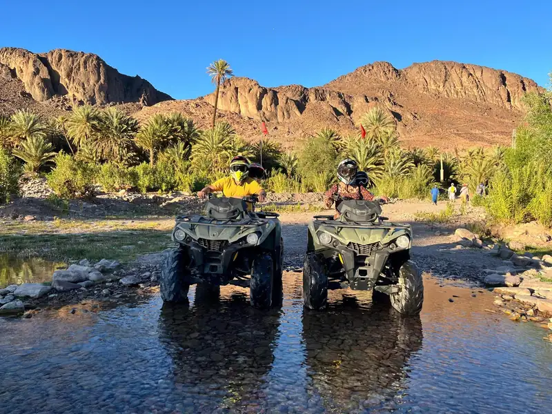 Two riders on quads crossing the river at Fint oasis near Ouarzazate
