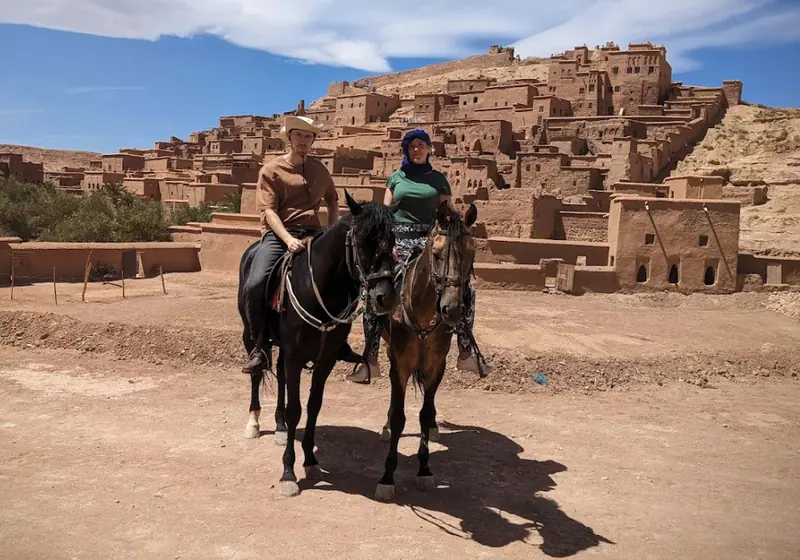 Two riders on horseback with the ksar of Ait Ben Haddou behind