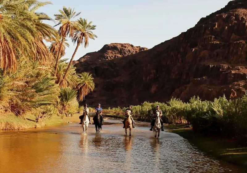 Riders on horseback crossing the river in Fint oasis